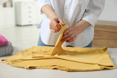 Photo of Woman folding clothes at white wooden table indoors, closeup