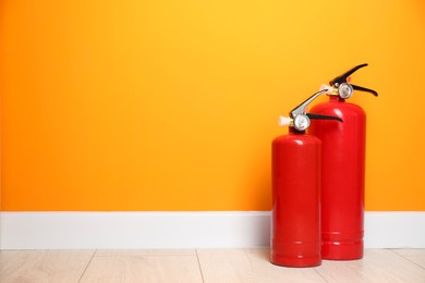 Fire extinguishers on floor near orange wall, space for text