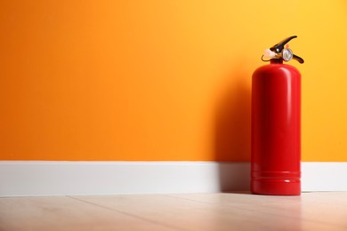 Photo of Fire extinguisher on floor near orange wall, space for text