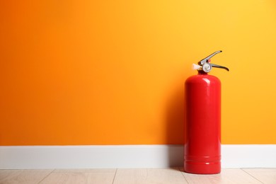 Photo of Fire extinguisher on floor near orange wall, space for text