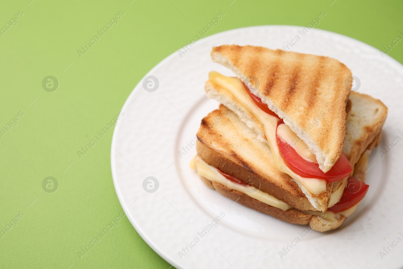 Photo of Pieces of toasted bread with melted cheese and tomato on green table, closeup. Space for text