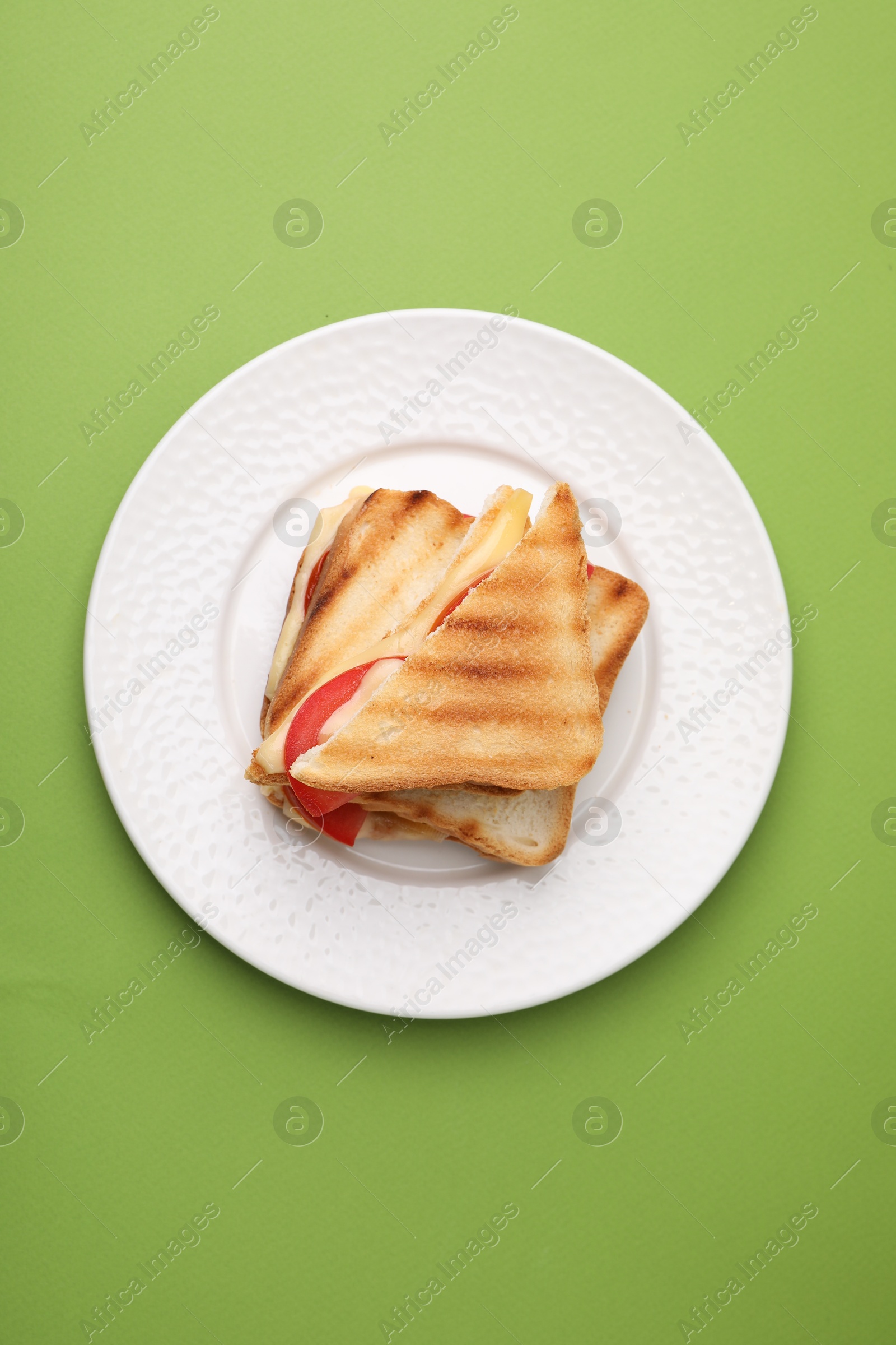 Photo of Pieces of toasted bread with melted cheese and tomato on green table, top view