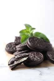 Tasty sandwich cookies and mint on white marble table