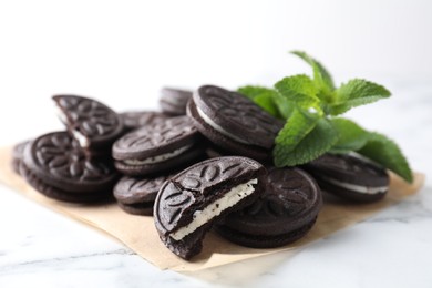 Tasty sandwich cookies and mint on white marble table