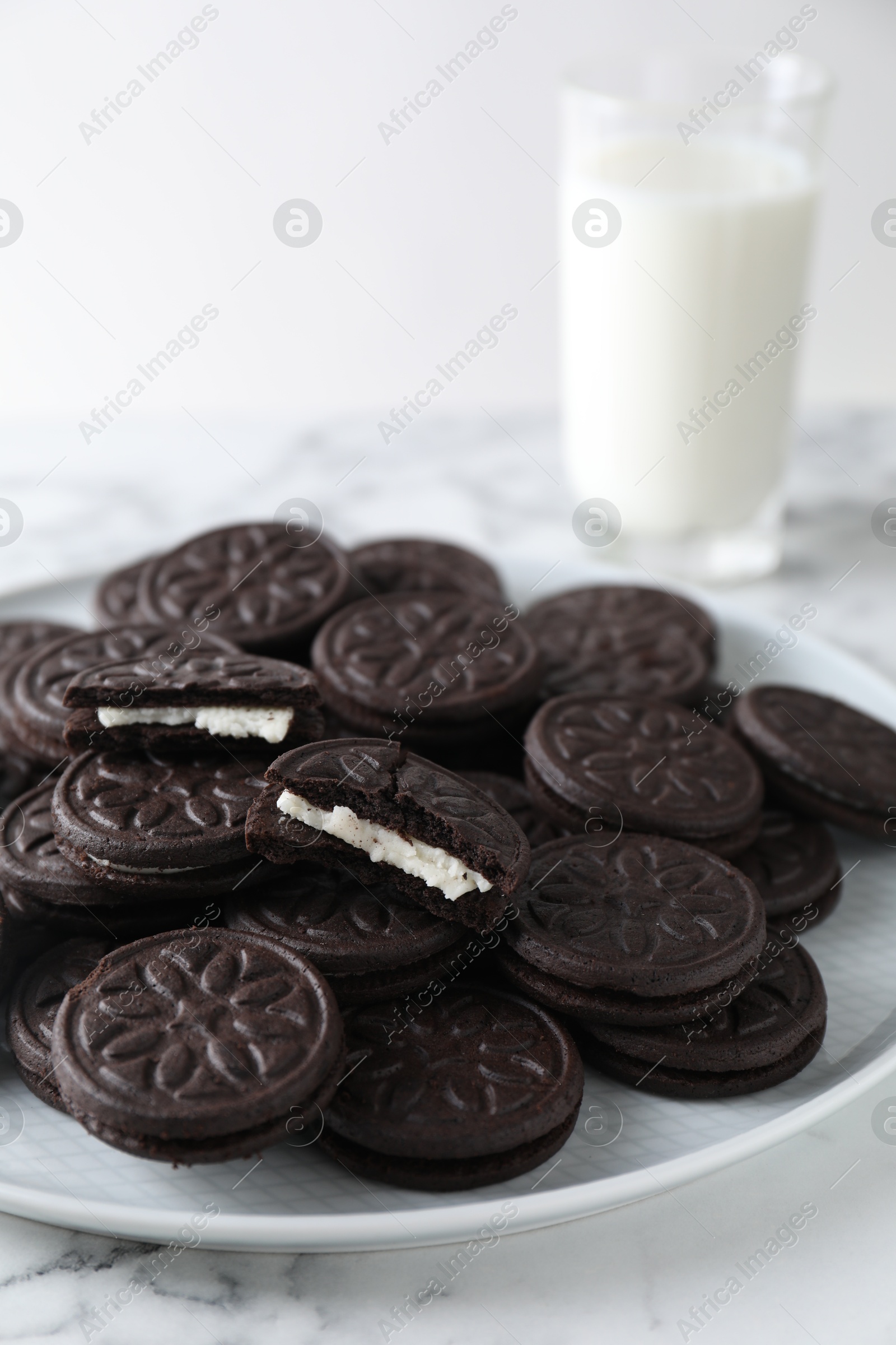 Photo of Tasty sandwich cookies and milk on white marble table