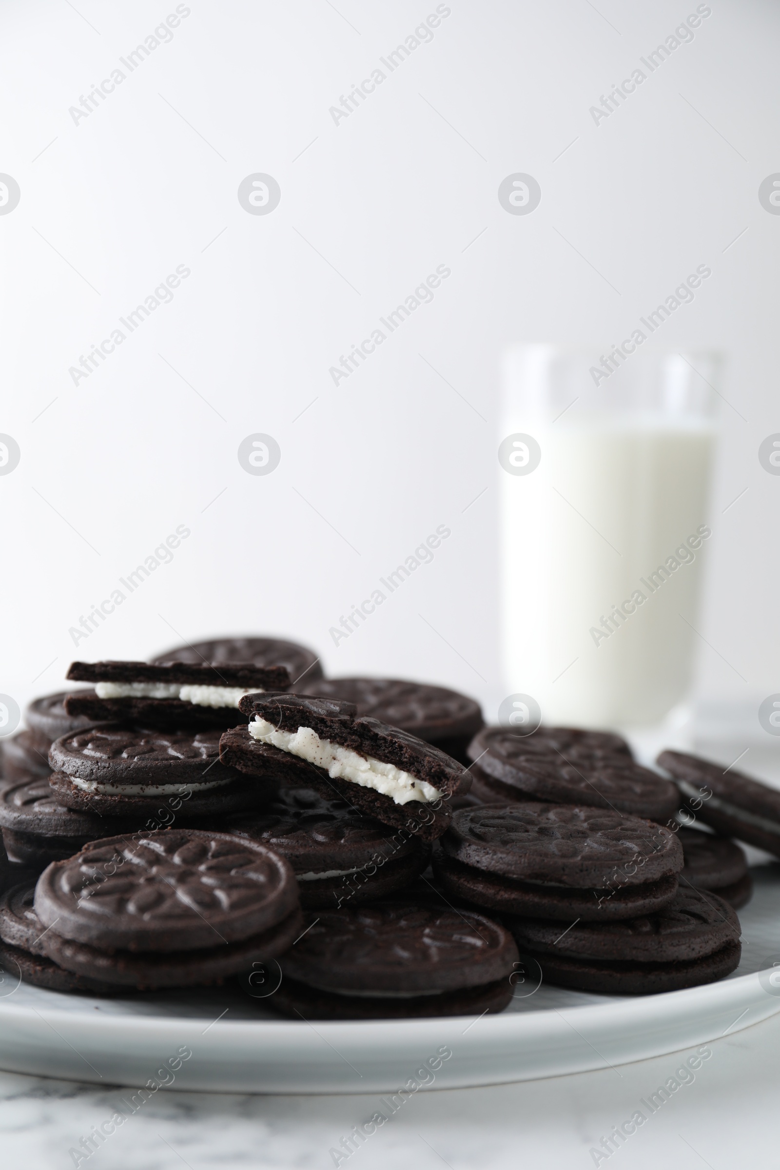 Photo of Tasty sandwich cookies and milk on white marble table