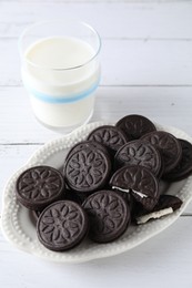 Tasty sandwich cookies and milk on white wooden table