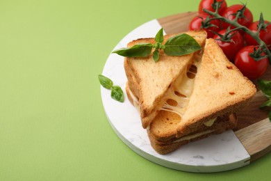 Photo of Pieces of toasted bread with melted cheese, tomatoes and basil on green background, space for text