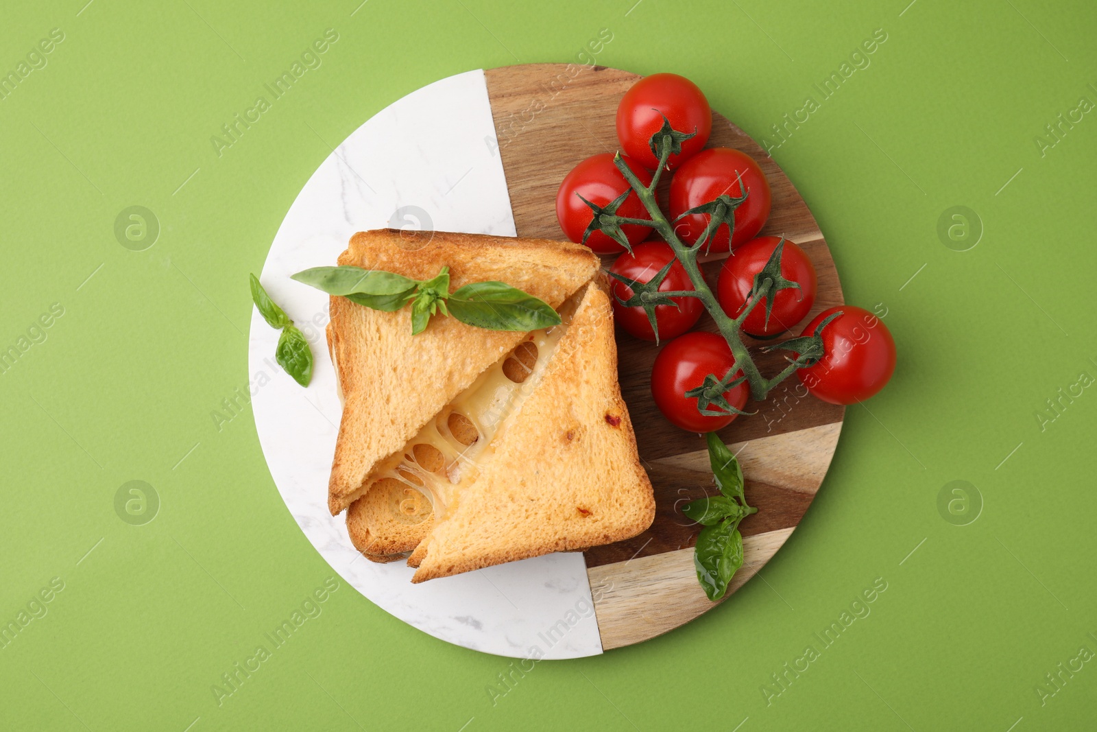 Photo of Pieces of toasted bread with melted cheese, tomatoes and basil on green background, top view