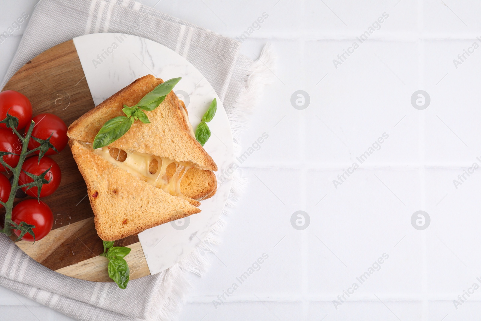 Photo of Pieces of toasted bread with melted cheese, tomatoes and basil on white tiled table, top view. Space for text