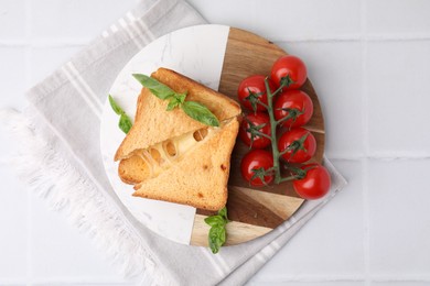 Photo of Pieces of toasted bread with melted cheese, tomatoes and basil on white tiled table, top view