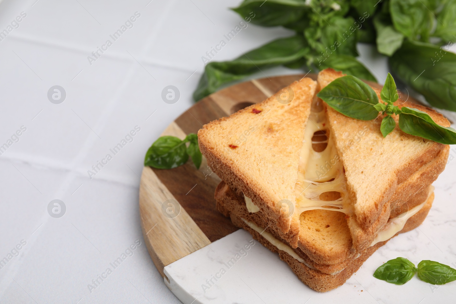 Photo of Pieces of toasted bread with melted cheese and basil on white tiled table. Space for text