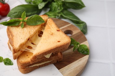 Photo of Pieces of toasted bread with melted cheese and basil on white table, closeup