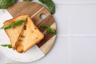 Photo of Pieces of toasted bread with melted cheese and basil on white tiled table, top view. Space for text