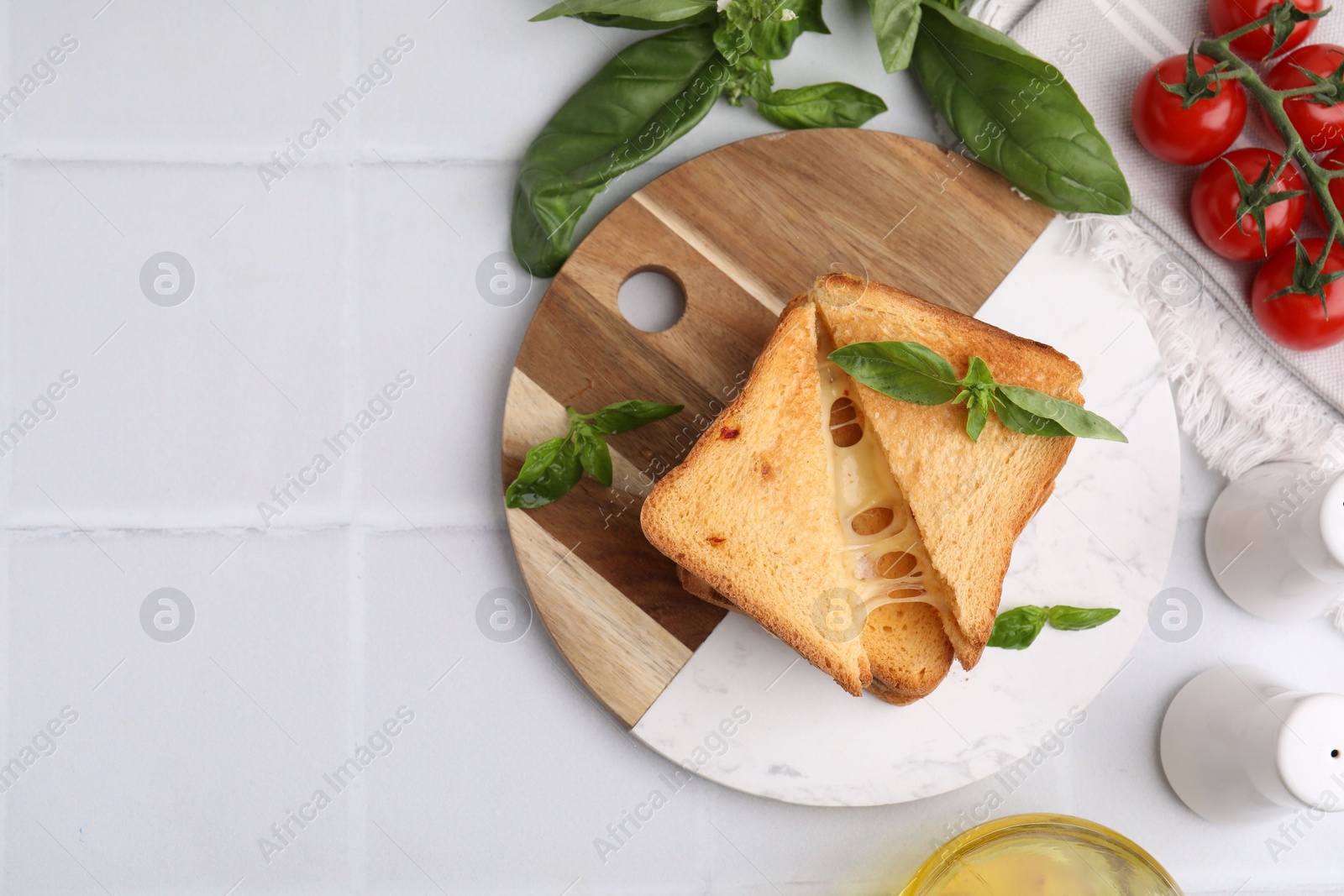 Photo of Pieces of toasted bread with melted cheese, tomatoes and basil on white tiled table, top view. Space for text