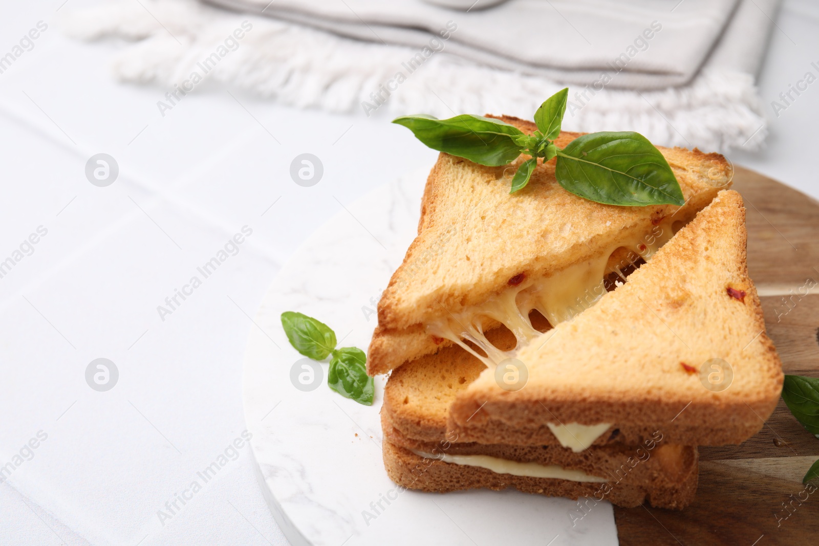 Photo of Pieces of toasted bread with melted cheese and basil on white table, space for text