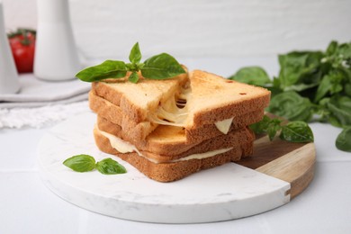 Pieces of toasted bread with melted cheese and basil on white table