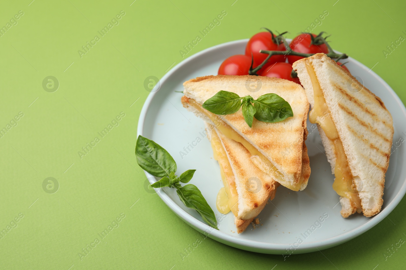 Photo of Pieces of toasted bread with melted cheese, tomatoes and basil on green background, space for text