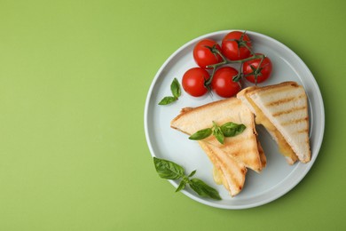 Photo of Pieces of toasted bread with melted cheese, tomatoes and basil on green background, top view. Space for text