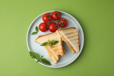 Photo of Pieces of toasted bread with melted cheese, tomatoes and basil on green background, top view