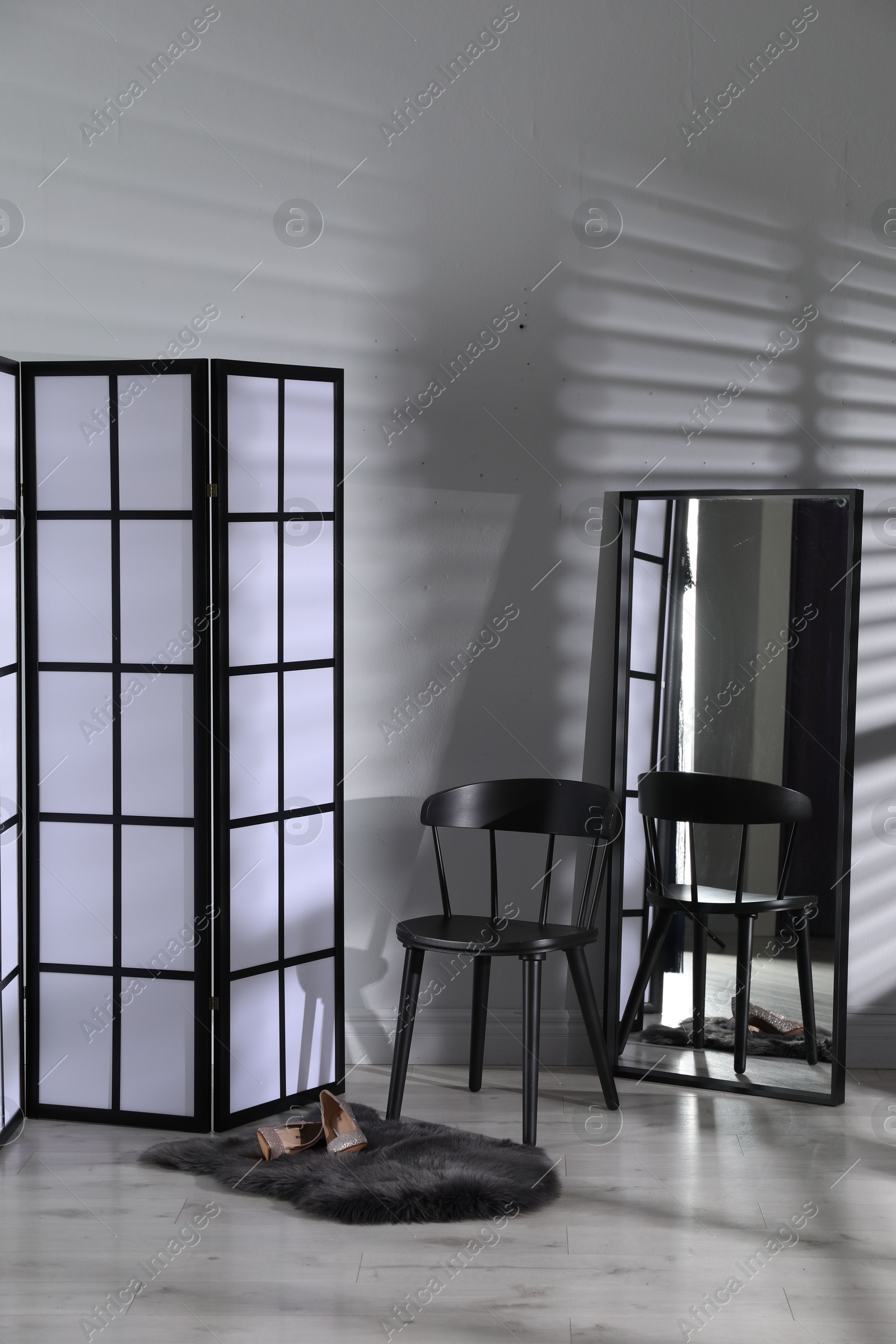 Photo of Folding screen, shoes, chair and mirror near white wall indoors