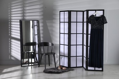 Folding screen, dress, shoes, chair and mirror near white wall indoors