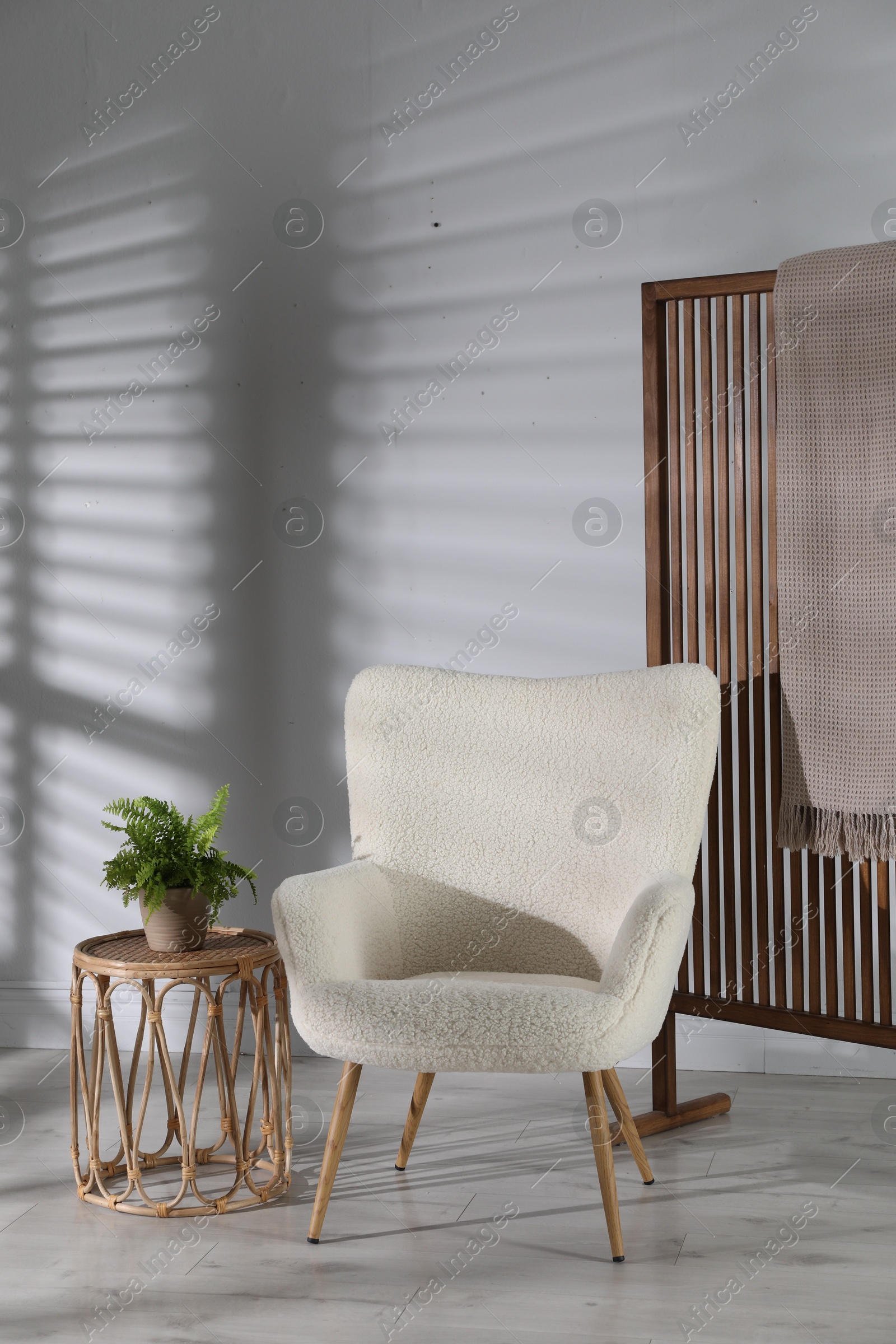 Photo of Wooden folding screen, blanket, armchair, side table and houseplant near light wall indoors