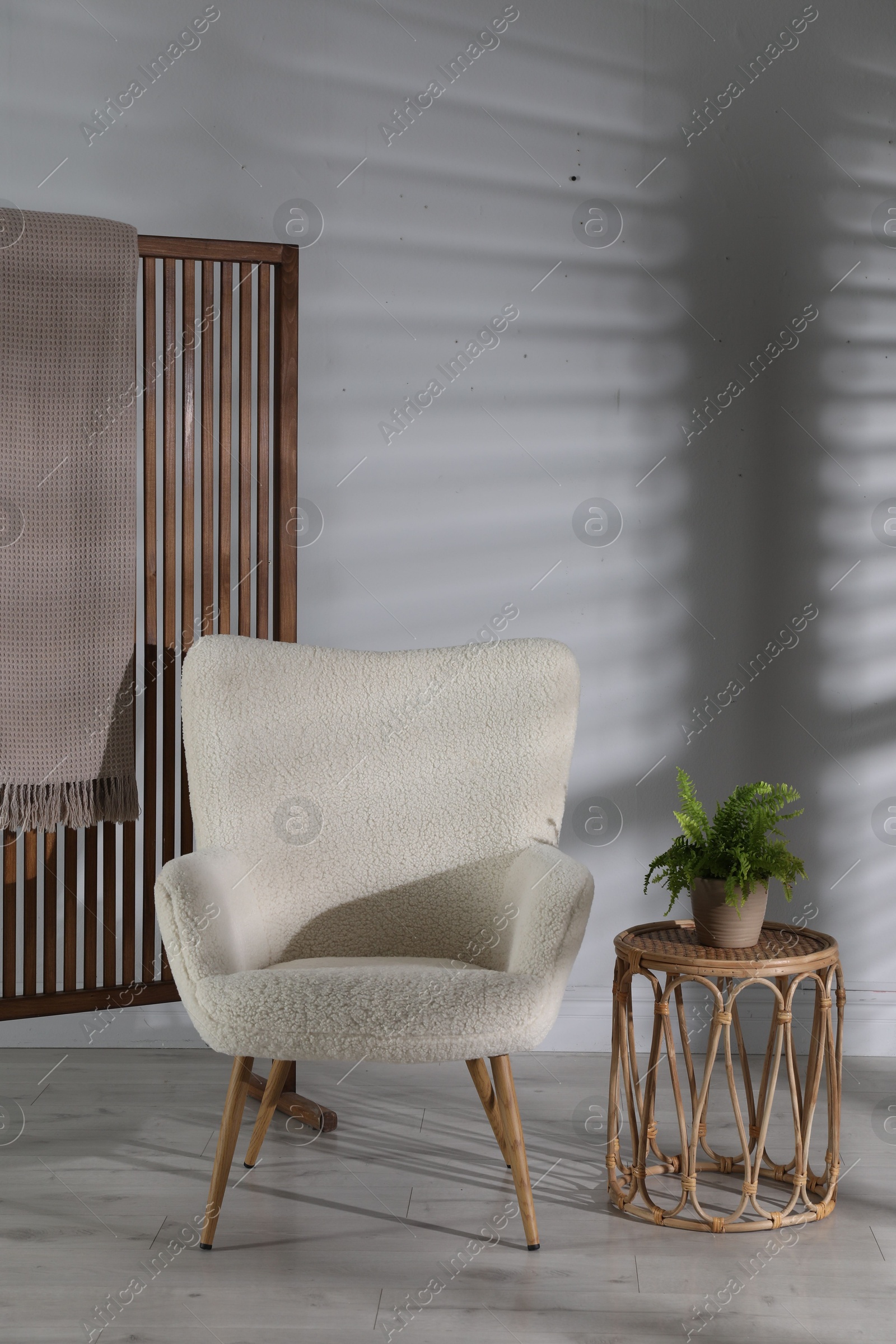 Photo of Wooden folding screen, blanket, armchair, side table and houseplant near light wall indoors