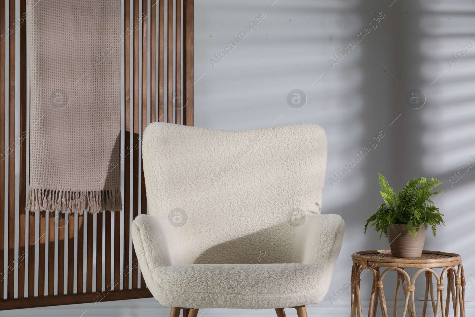 Photo of Wooden folding screen, blanket, armchair, side table and houseplant near light wall indoors