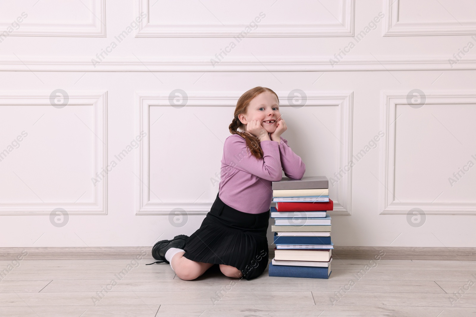 Photo of Smiling girl with stack of books on floor indoors