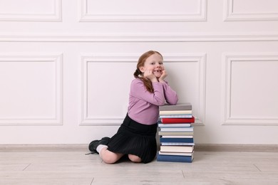 Smiling girl with stack of books on floor indoors
