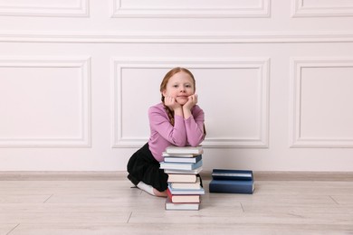 Photo of Little girl with stack of books on floor indoors