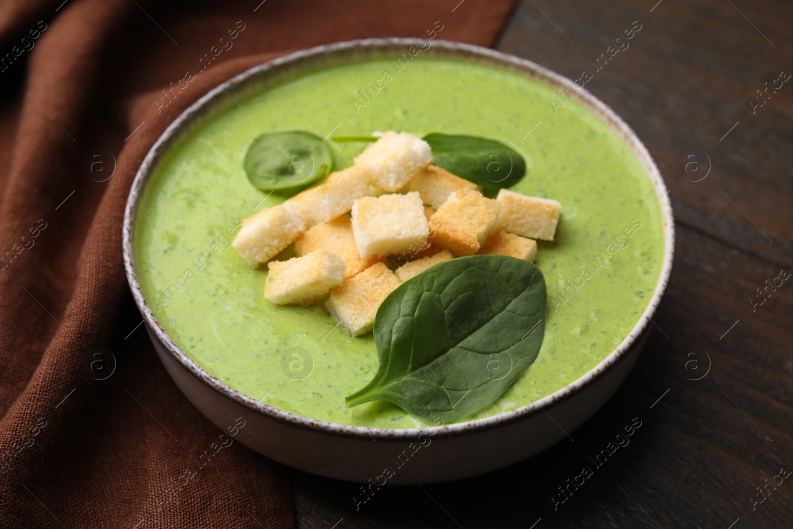 Photo of Delicious spinach cream soup with leaves and croutons in bowl on wooden table