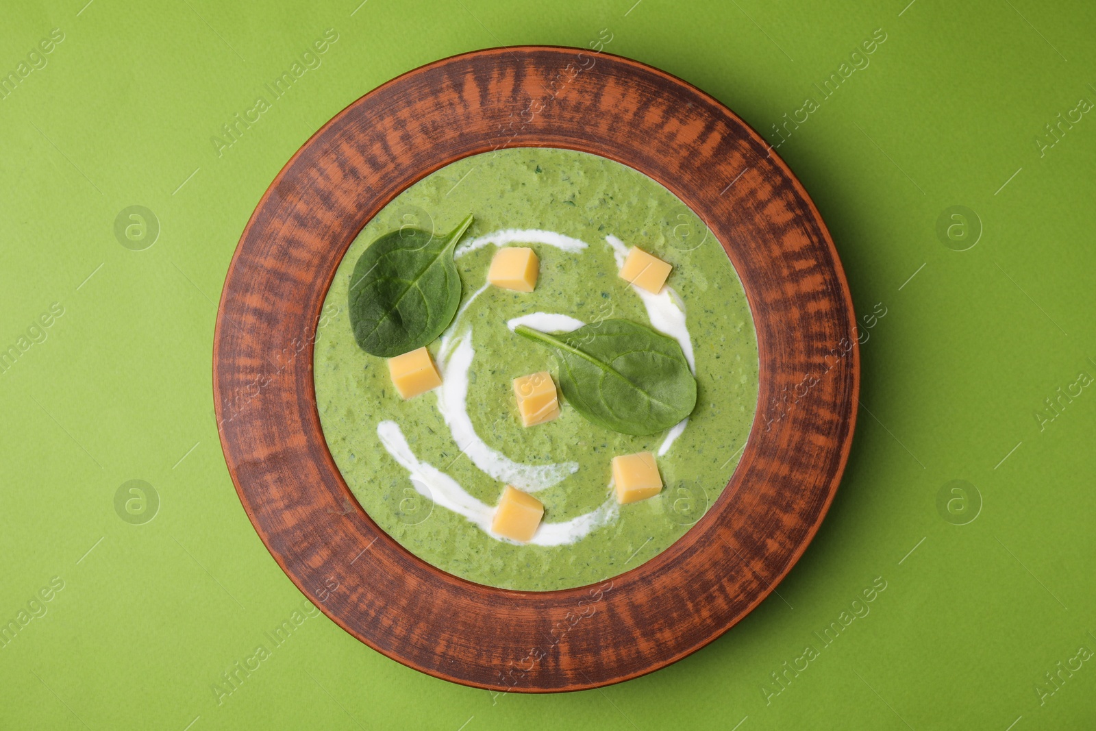 Photo of Delicious spinach cream soup with leaves and cheese in bowl on green background, top view