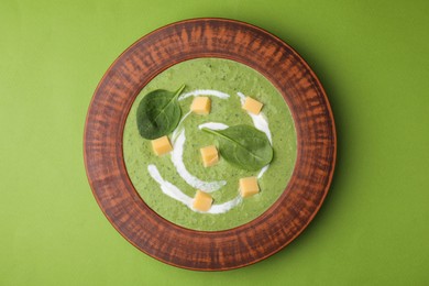 Photo of Delicious spinach cream soup with leaves and cheese in bowl on green background, top view