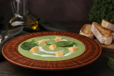 Photo of Delicious spinach cream soup with leaves and cheese in bowl on wooden table, closeup