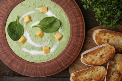 Photo of Delicious spinach cream soup with leaves and cheese in bowl on wooden table, flat lay