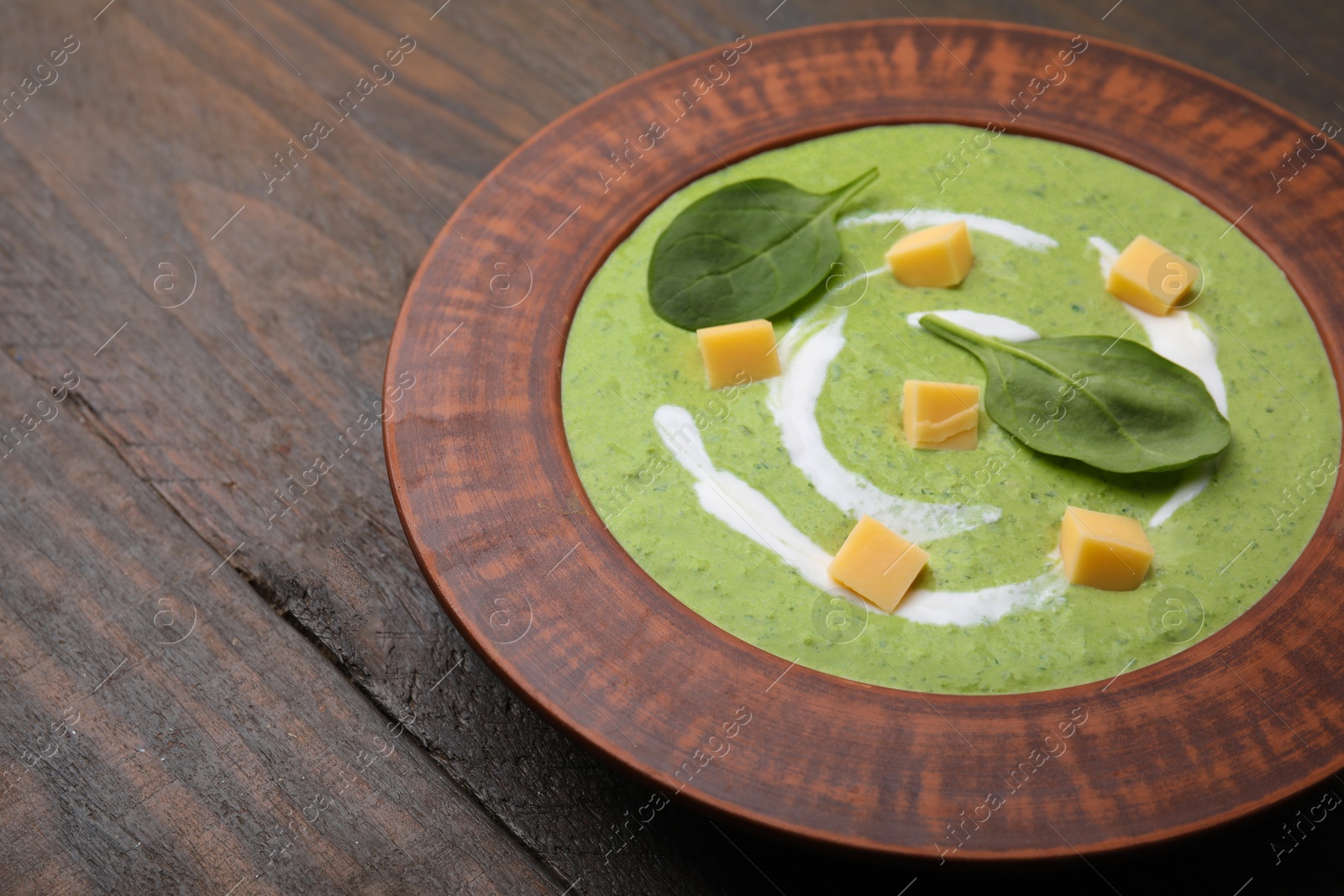 Photo of Delicious spinach cream soup with leaves and cheese in bowl on wooden table, closeup. Space for text