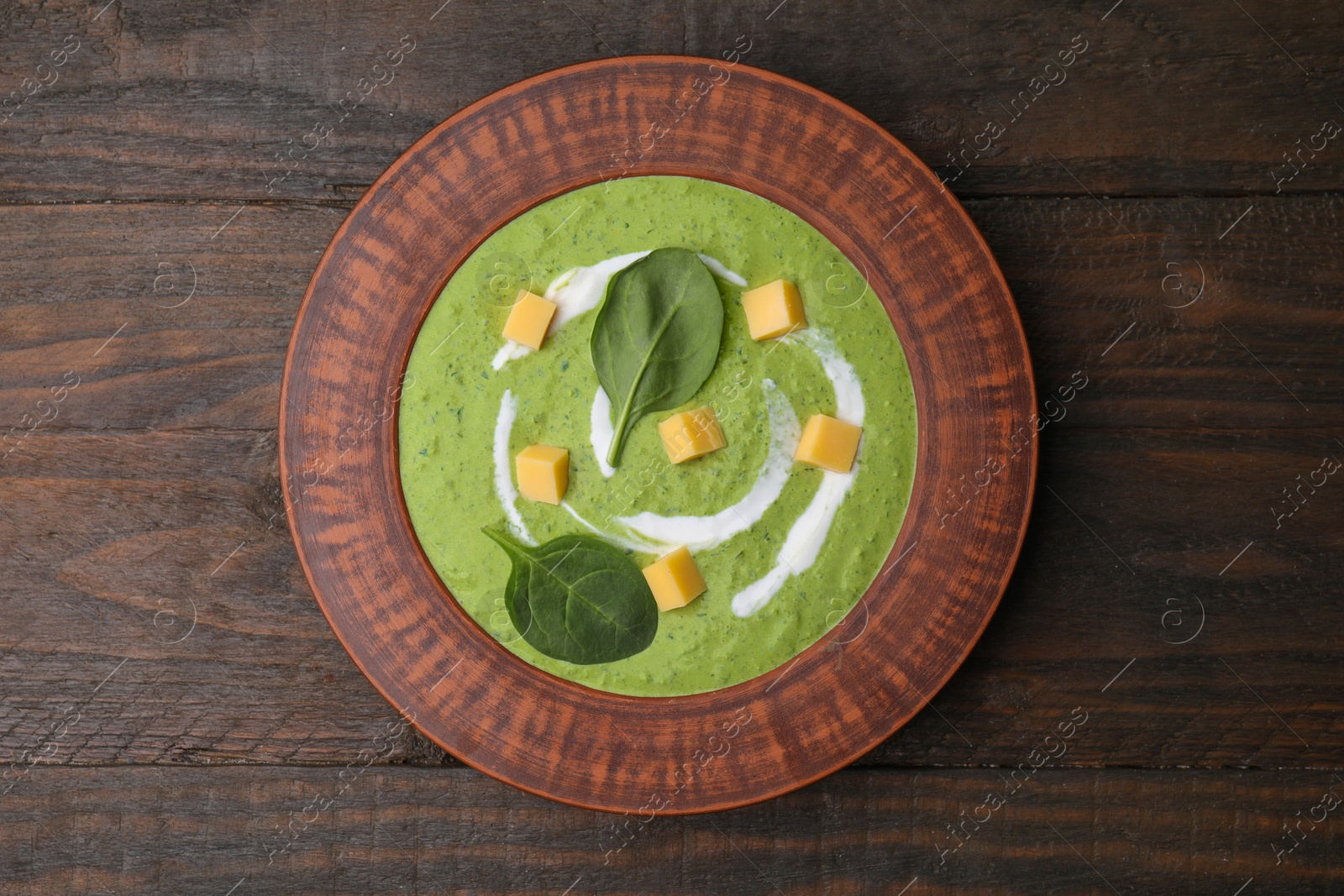 Photo of Delicious spinach cream soup with leaves and cheese in bowl on wooden table, top view