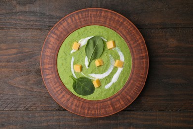 Photo of Delicious spinach cream soup with leaves and cheese in bowl on wooden table, top view