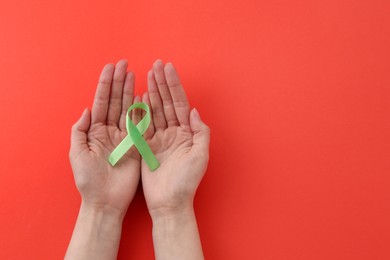 Woman with light green awareness ribbon on red background, top view. Space for text