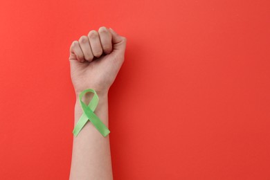 Photo of Woman with light green awareness ribbon on red background, top view. Space for text