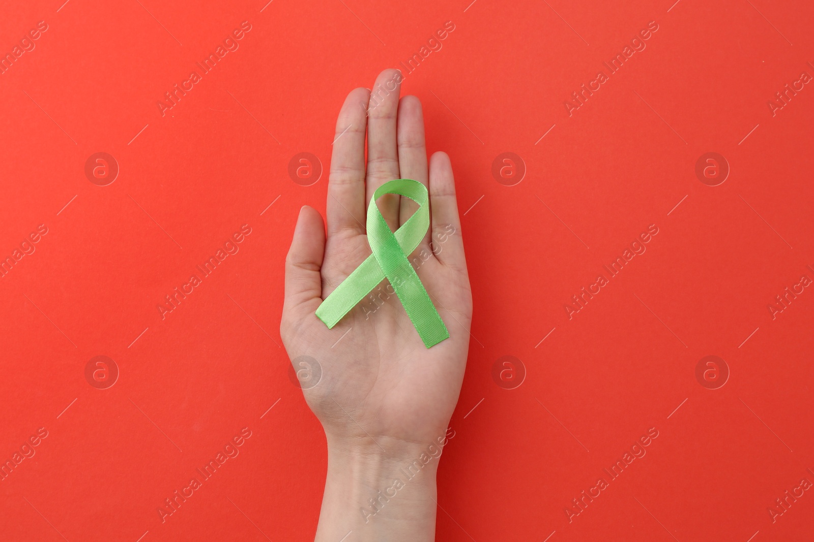 Photo of Woman with light green awareness ribbon on red background, top view