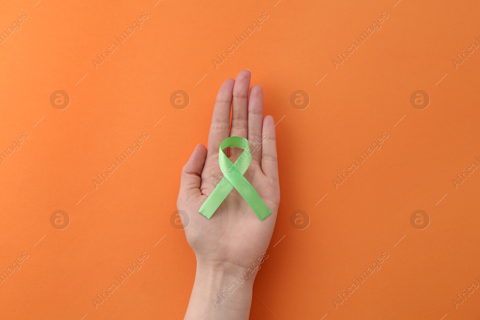 Photo of Woman with green awareness ribbon on orange background, top view