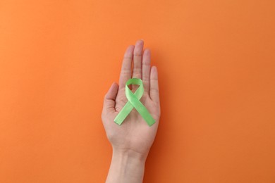 Woman with green awareness ribbon on orange background, top view