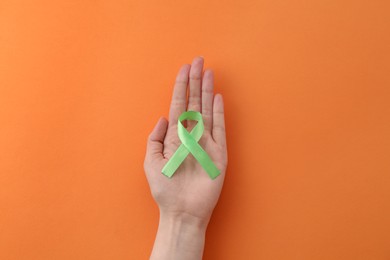 Photo of Woman with green awareness ribbon on orange background, top view