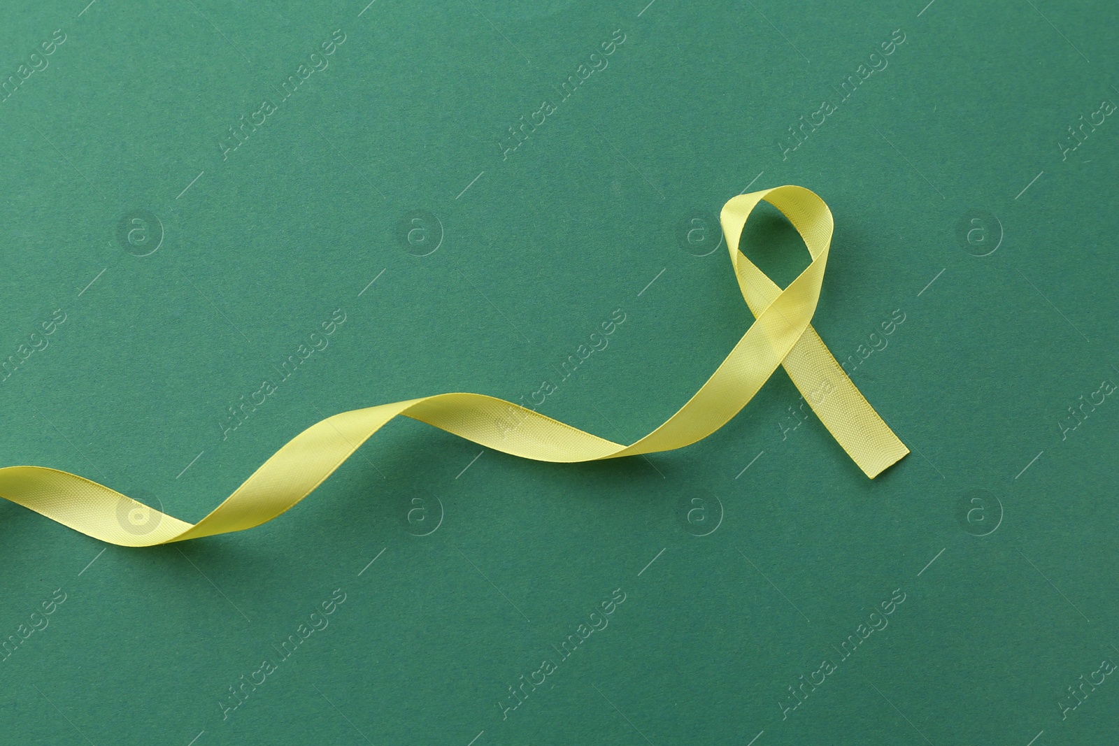 Photo of Yellow awareness ribbon on green background, top view