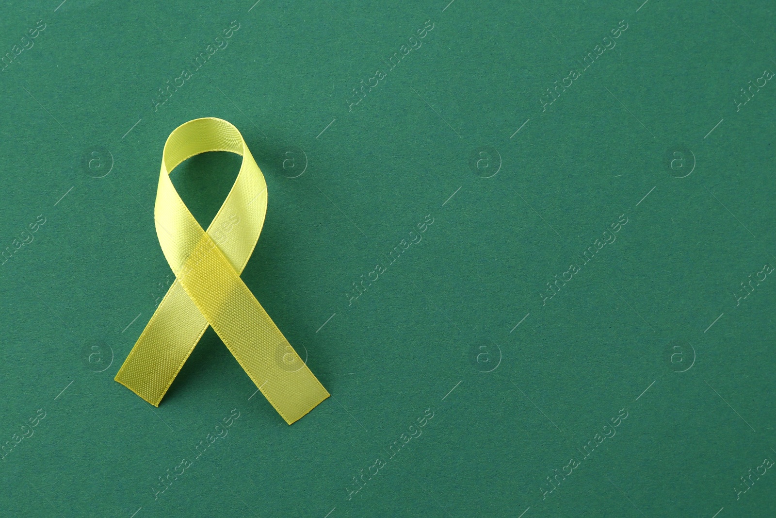 Photo of Yellow awareness ribbon on green background, top view. Space for text