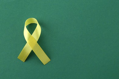 Photo of Yellow awareness ribbon on green background, top view. Space for text
