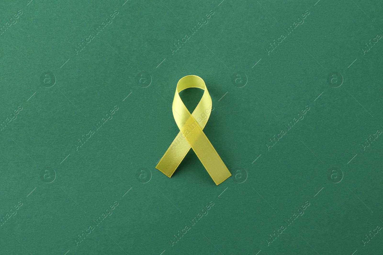 Photo of Yellow awareness ribbon on green background, top view